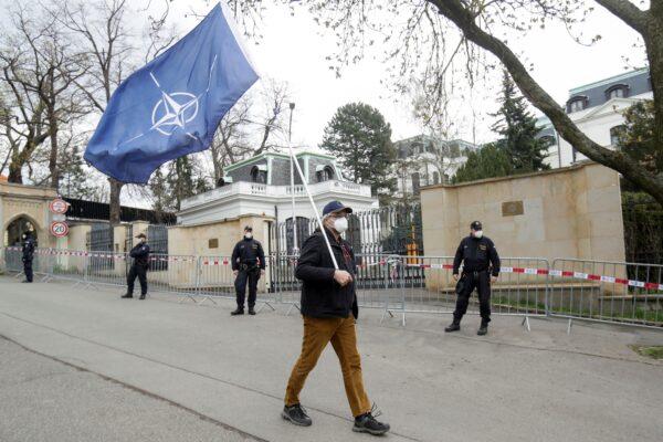 A man carrying a NATO flag walks past police officers outside the Russian Embassy in Prague, Czech Republic, on Apr. 18, 2021. (David W Cerny/Reuters)