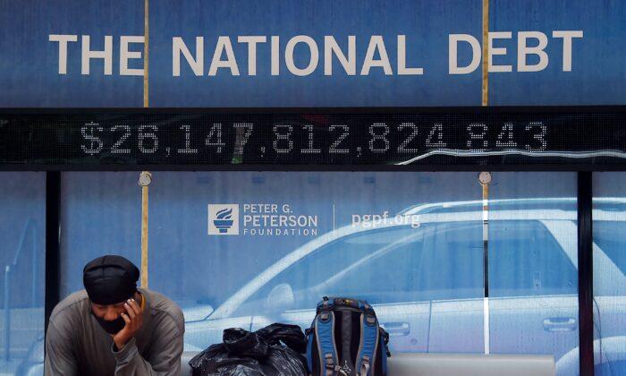 A man waits at a bus stop that displays the official national debt of the United States in Washington on June 19, 2020. (Olivier Douliery/AFP via Getty Images)