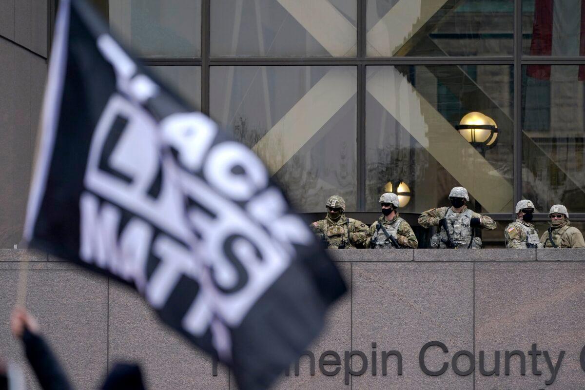 National Guard members are seen as a person flies a Black Lives Matter flag during a rally after the murder trial against former Minneapolis police officer Derek Chauvin advanced to jury deliberations outside of the Hennepin County Government Center in Minneapolis, Minn., on April 19, 2021. (Julio Cortez/AP Photo)
