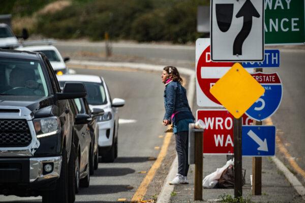A homeless woman asks drivers for assistance in Oceanside, Calif., on April 14, 2021. (John Fredricks/The Epoch Times)