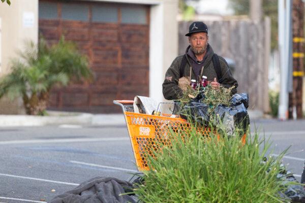 A homeless person stands next to his cart in a parking lot in Oceanside, Calif., on April 14, 2021. (John Fredricks/The Epoch Times)