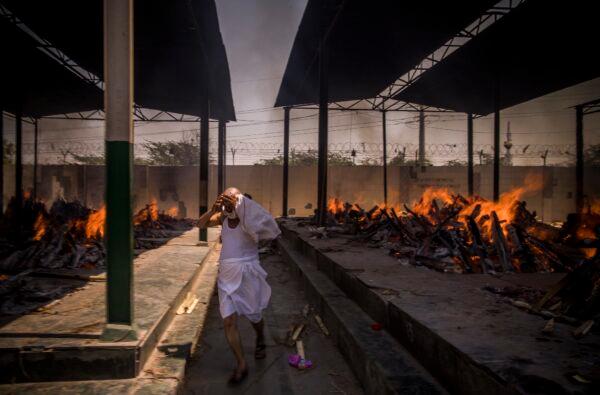 A priest who helps to perform last rites runs while covering his face amid the multiple burning funeral pyres of patients who died of the COVID-19 coronavirus disease at a crematorium in New Delhi, India, on April 24, 2021. (Anindito Mukherjee/Getty Images)