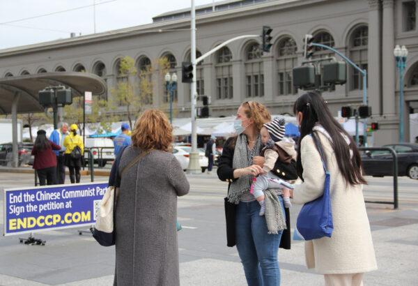 WeiQun Hua (R) explains to pedestrians that the rally is to commemorate the peaceful appeal and raise awareness about the persecution still happening in China today, in front of the Ferry Building in San Francisco on April 24, 2021. (David Lam/The Epoch Times)