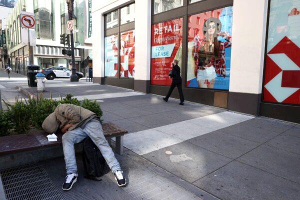 A homeless person sleeps on a bench in front of closed retail stores in San Francisco on April 16, 2021. (Justin Sullivan/Getty Images)