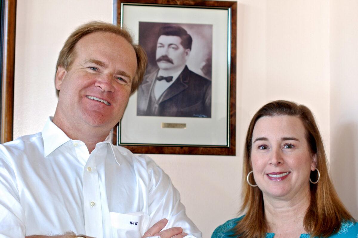 Robert J. Whann IV, known as Sandy, and Katherine Whann, in front of a photo of George Leidenheimer. (Photograph taken by the Southern Foodways Alliance)