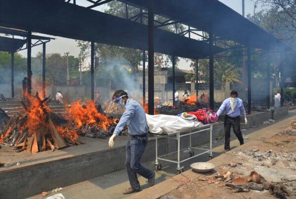 Relatives carry the body of a person who died of COVID-19 as multiple pyres of other COVID-19 victims burn at a crematorium in New Delhi, India on May 1, 2021. (Amit Sharma/AP Photo)