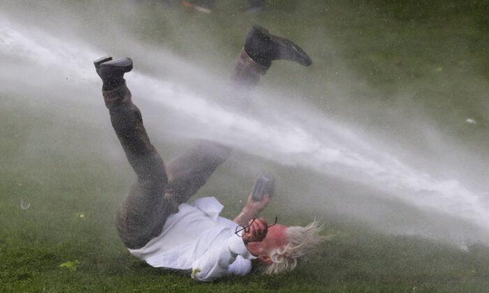 A man is doused by a water cannon during clashes as people gather at the Bois de la Cambre/Ter Kamerenbos park for a party called "La Boum 2" in defiance of Belgium's CCP virus disease (COVID-19) social distancing measures and restrictions, in Brussels on May 1, 2021. (Yves Herman/Reuters)