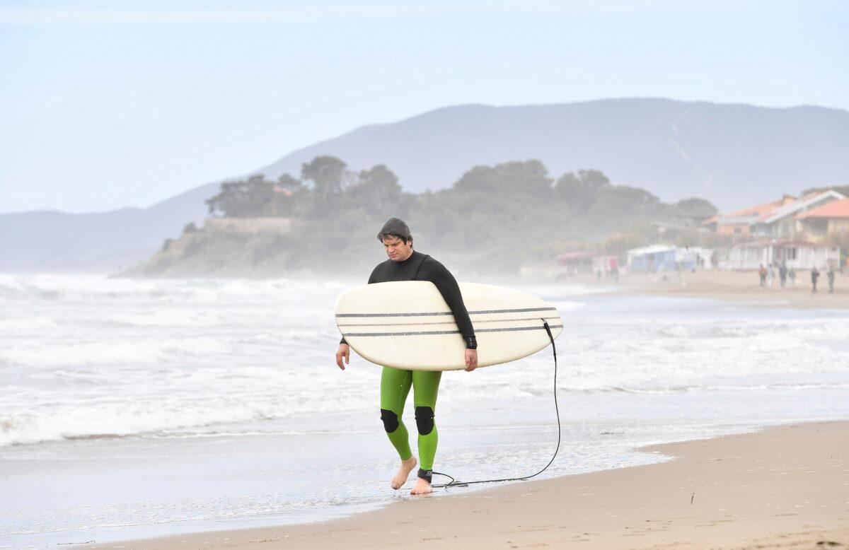 A surfer walks on the beach as COVID-19 restrictions ease around the country, in Castiglione della Pescaia, Italy, on May 2, 2021. (Jennifer Lorenzini/Reuters)