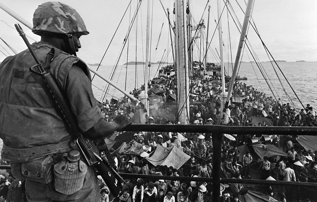 A picture released on May 5, 1975 shows an American soldier watching South Vietnamese refugees crowding a U.S. Navy boat off the coasts of Vietnam at the end of the Vietnamese war. (AFP via Getty Images)