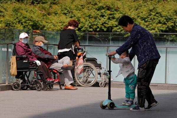 A woman plays with a child near elderly people on wheelchairs sunbathing on a compound of a commercial office building in Beijing on May 10, 2021. (AP Photo/Andy Wong)