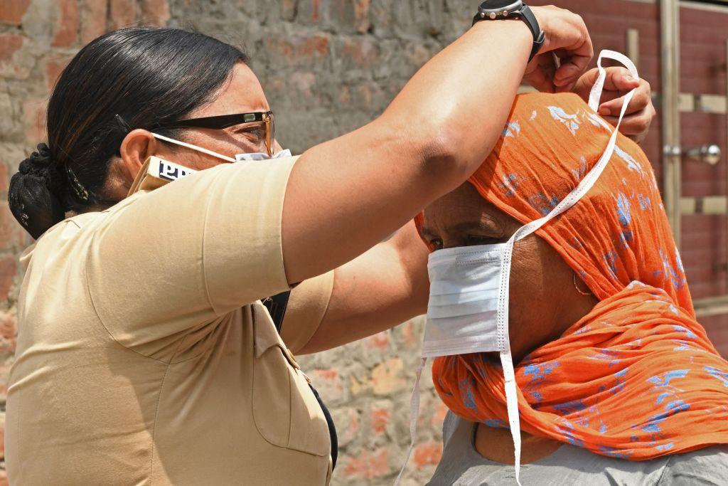 A police officer ties a facemask on a woman after police in rural areas launched a free cab service for villagers to the COVID-19 coronavirus testing and vaccination centers on the outskirts of Amritsar, India, on May 3, 2021. (Narinder Nanu / AFP)