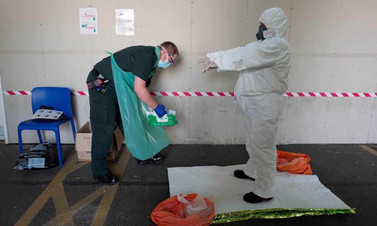 Paramedic Kate Donne (R) is guided through the safe removal of her PPE3-level clothing in the ambulance bay of Southampton General hospital after treating a patient with possible COVID-19 symptoms in England on May 6, 2020. (Leon Neal/Pool/AFP via Getty Images)