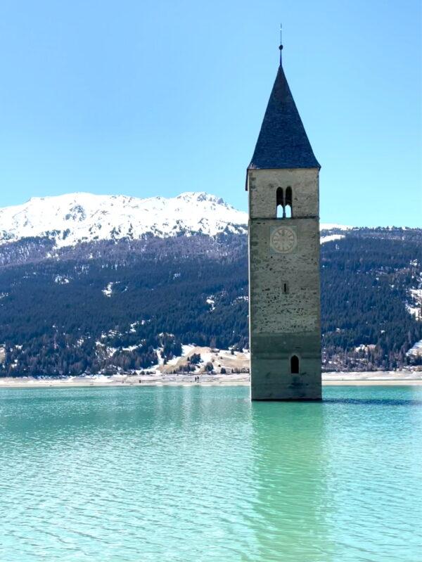 A screengrab from a video of a church bell tower emerging alone from a lake, as it is drained for repair works of a hydroelectric plant, that replaced the village of Curon 71 years ago, at Resia Lake, Italy on April 24, 2021. (Luisa Azzolini/Handout via Reuters)