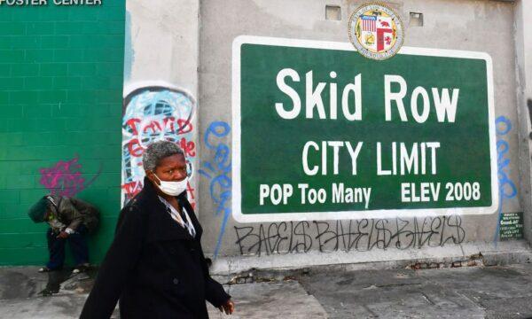 A woman walks past a Skid Row sign pointing out a population of "Too Many" in Los Angeles, on April 26, 2021. (Frederic J. Brown/AFP via Getty Images)