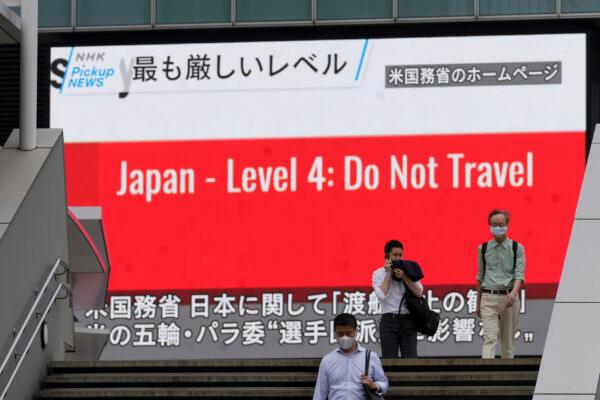 People walk in front of a screen showing the news on U.S. warning against visits to Japan, in Tokyo on May 25, 2021. (Eugene Hoshiko/AP Photo)