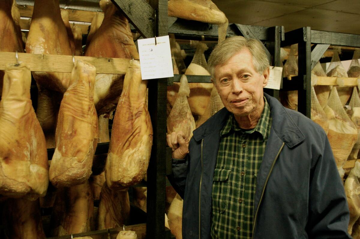 Allan Benton in front of racks of hanging country hams. (Sara Wood/Southern Foodways Alliance)