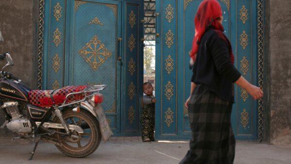 A child looks out from a door as a Uighur woman walks by in a residential area in Turpan, Xinjiang Uighur Autonomous Region, on Oct. 31, 2013. (Michael Martina/Reuters)