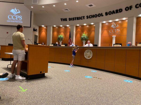 Dan Cook addresses the Collier County School Board regarding his concerns of CRT content in textbooks as his daughter Selah distributes Pocket Constitution booklets to each member in the district’s classrooms, on May 7, 2021. (Patricia Tolson/The Epoch Times)