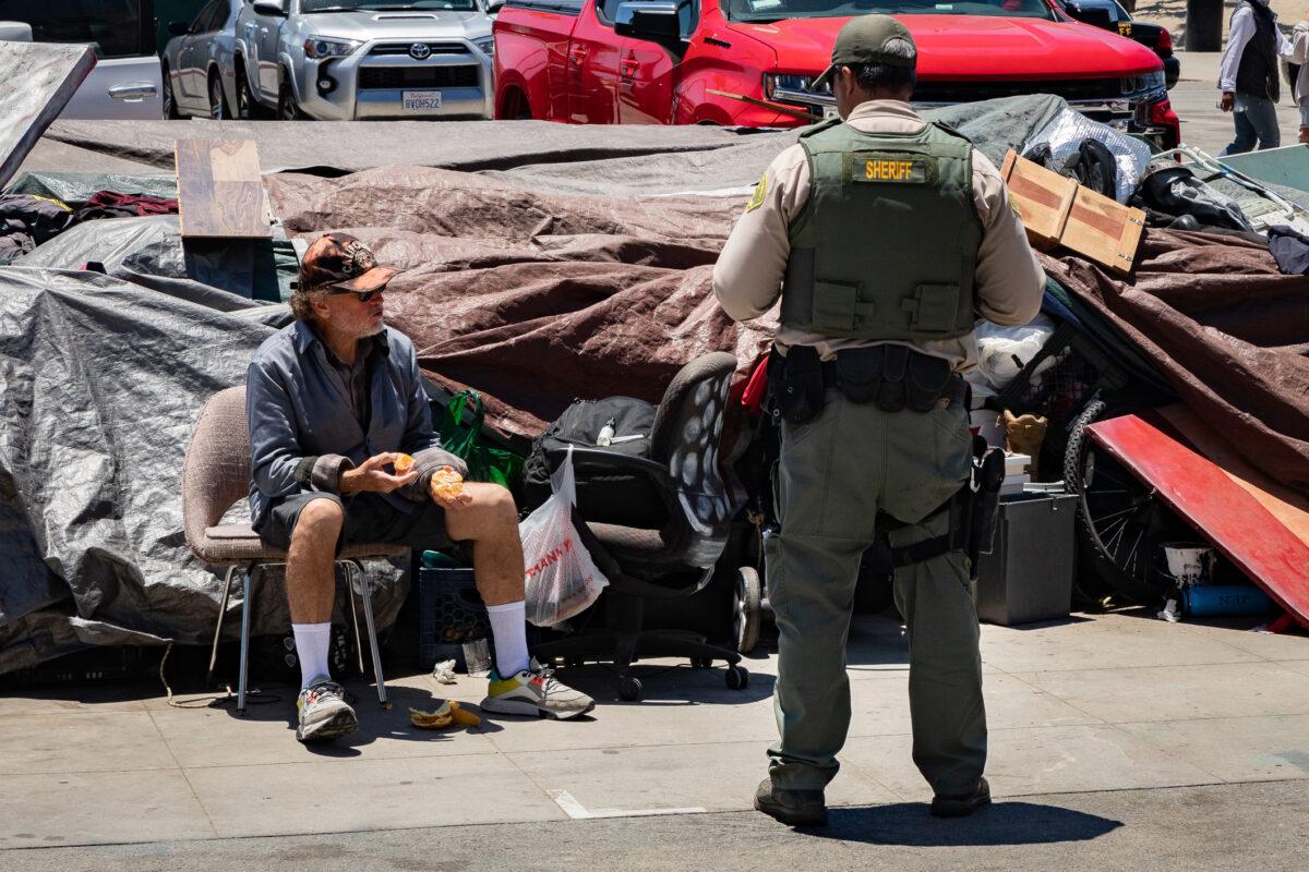 A deputy from the Los Angeles Sheriff’s Department speaks to a homeless man sitting in front of his encampment in Venice, Calif., on June 8, 2021. (John Fredricks/The Epoch Times)