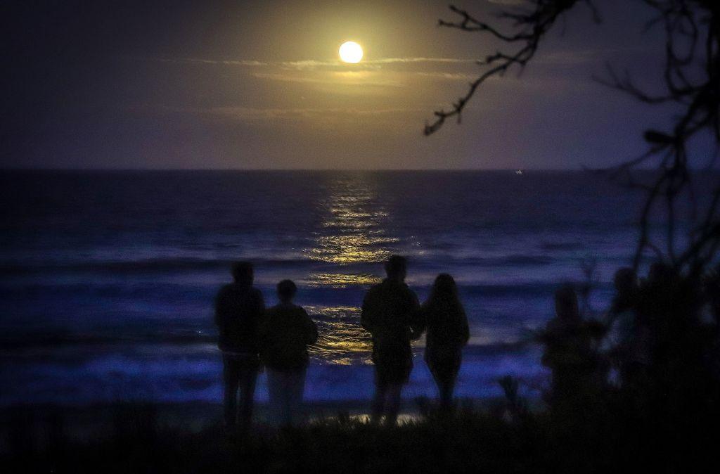 People watch the Strawberry Moon rise over the ocean on Narrawallee Beach, near Mollymook on the south coast of New South Wales, on June 6, 2020. (David Gray/AFP via Getty Images)