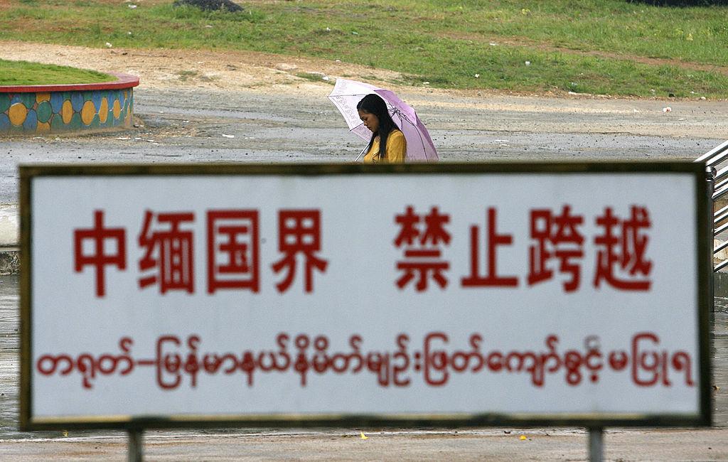 A Burmese woman walks behind a warning sign along the boundary line in the China-Burma border town of Wanding, in China's southwestern province of Yunnan, on Sept. 27, 2007. (STR/AFP via Getty Images)
