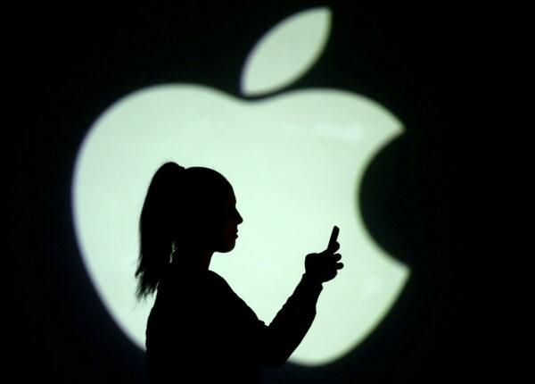 Silhouette of a mobile user seen next to a screen projection of the Apple logo in this picture illustration taken March 28, 2018. (Dado Ruvic/Illustration/Reuters)
