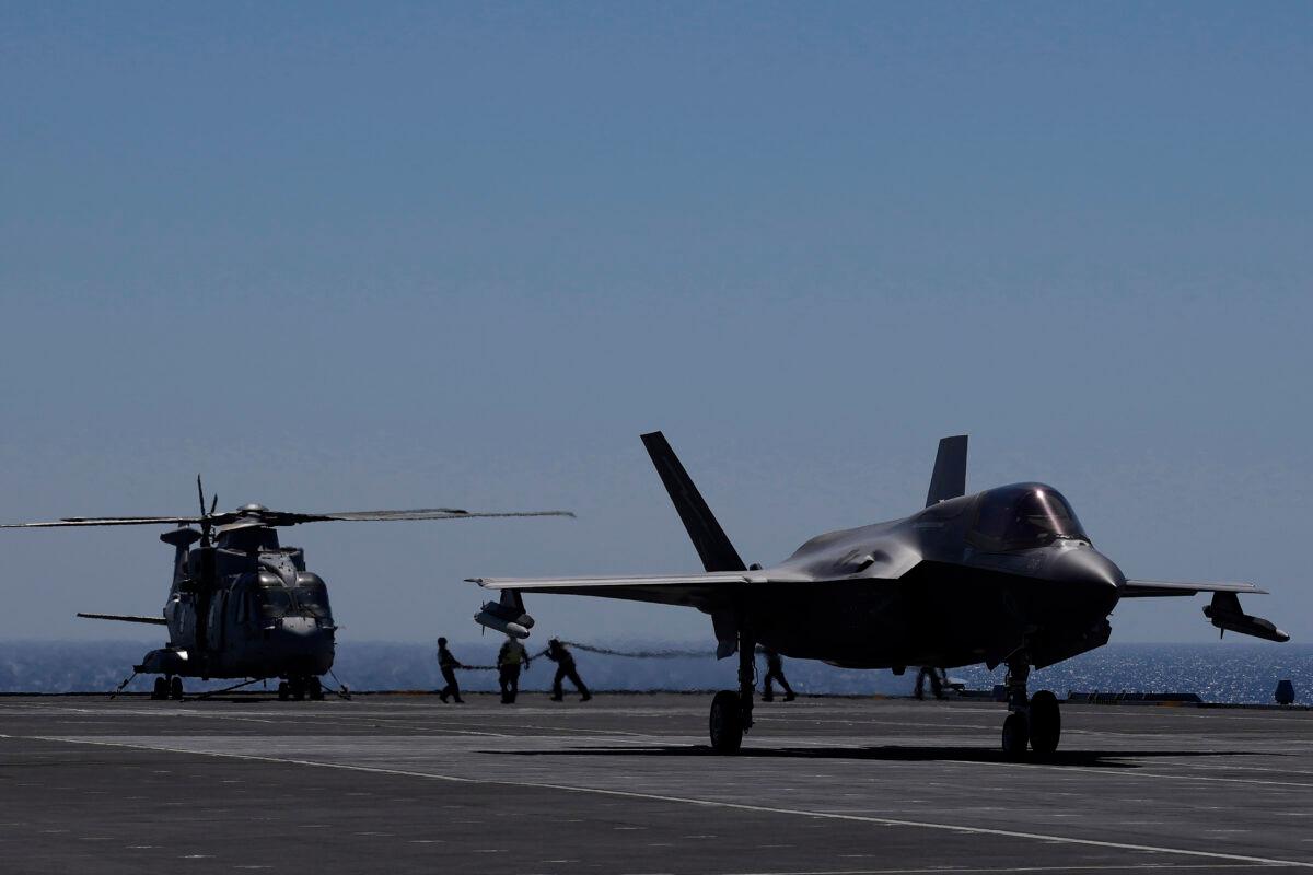 Crew members carry a pipe to refuel a helicopter as an F-35 aircraft prepares for take off on the UK's aircraft carrier HMS Queen Elizabeth in the Mediterranean Sea on Sunday, June 20, 2021. (Petros Karadjias/AP)