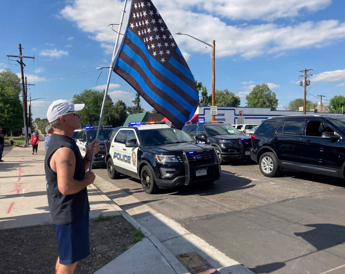 John Garrod, of Arvada, stands holding a blue line flag at the beginning of a line of about 30 police cars lined up for a procession in honor of the officer who was fatally shot in Arvada, Colo., on June 21, 2021. (Colleen Slevin/AP Photo)