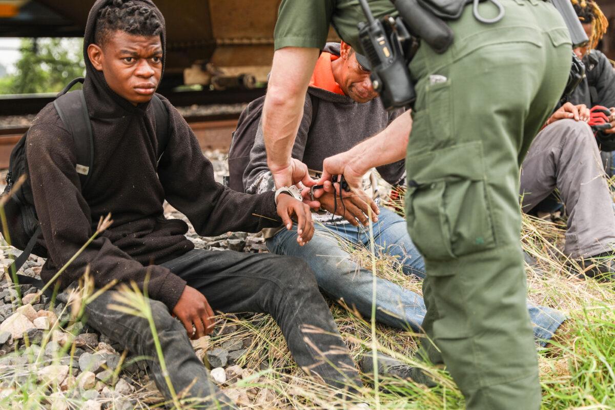A Border Patrol agent handcuffs illegal aliens together after they jumped off a train and tried to evade apprehension near Uvalde, Texas, on June 21, 2021. (Charlotte Cuthbertson/The Epoch Times)