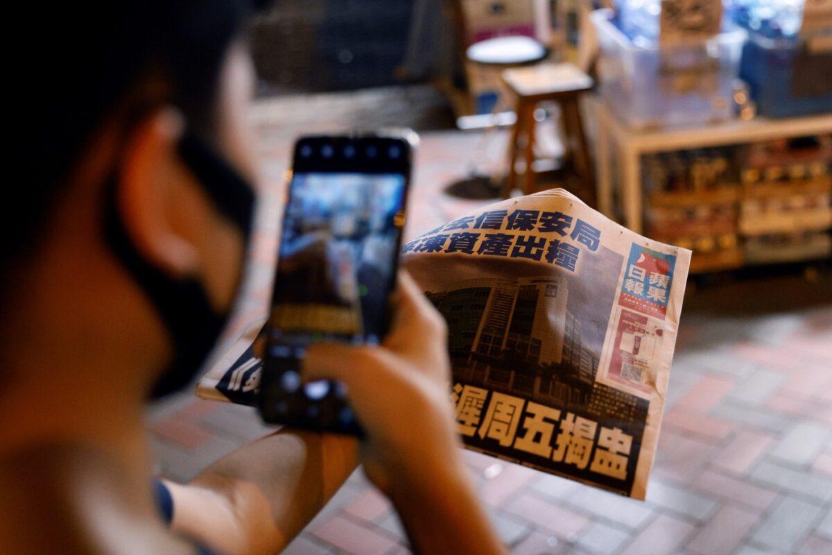 A man takes a photo of his copy of the Apple Daily newspaper after it looked set to close for good by Saturday following police raids and the arrest of executives in Hong Kong, on June 22, 2021. (Tyrone Siu/File/Reuters)