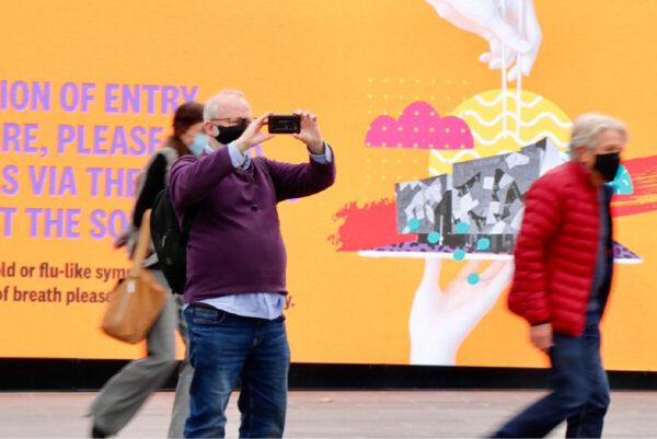 A pedestrian takes a photo of the rally boycotting Beijing's 2022 Winter Olympics in Melbourne, Australia, on June 23, 2021. (The Epoch Times)