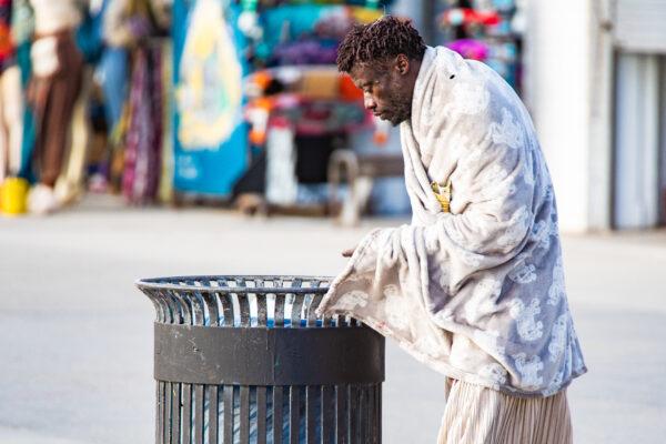 A homeless man looks for food in a trash can in Venice Beach, Calif., on Jan. 27, 2021. (John Fredricks/The Epoch Times)