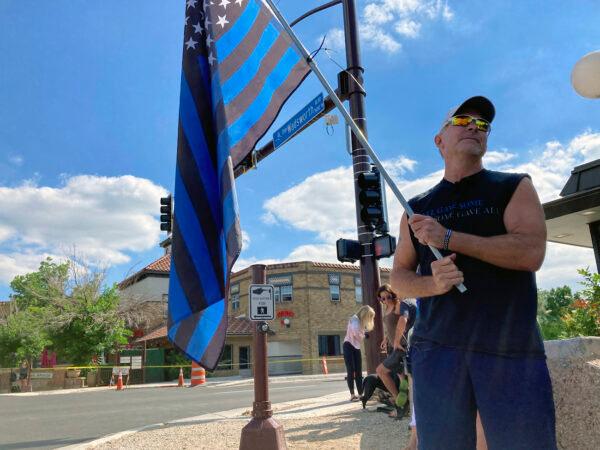 A man holds a thin blue line flag at the beginning of a line of about 30 police cars lined up for a procession in honor of the officer who was fatally shot in Arvada, Colo., on June 21, 2021. (Colleen Slevin/AP Photo)