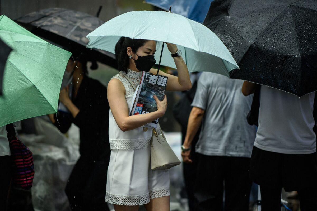A woman protects her copy of the Apple Daily newspaper's final issue from the rain after lining up to buy it from a newsstand in Hong Kong on June 24, 2021. (Anthony Wallace/AFP via Getty Images)