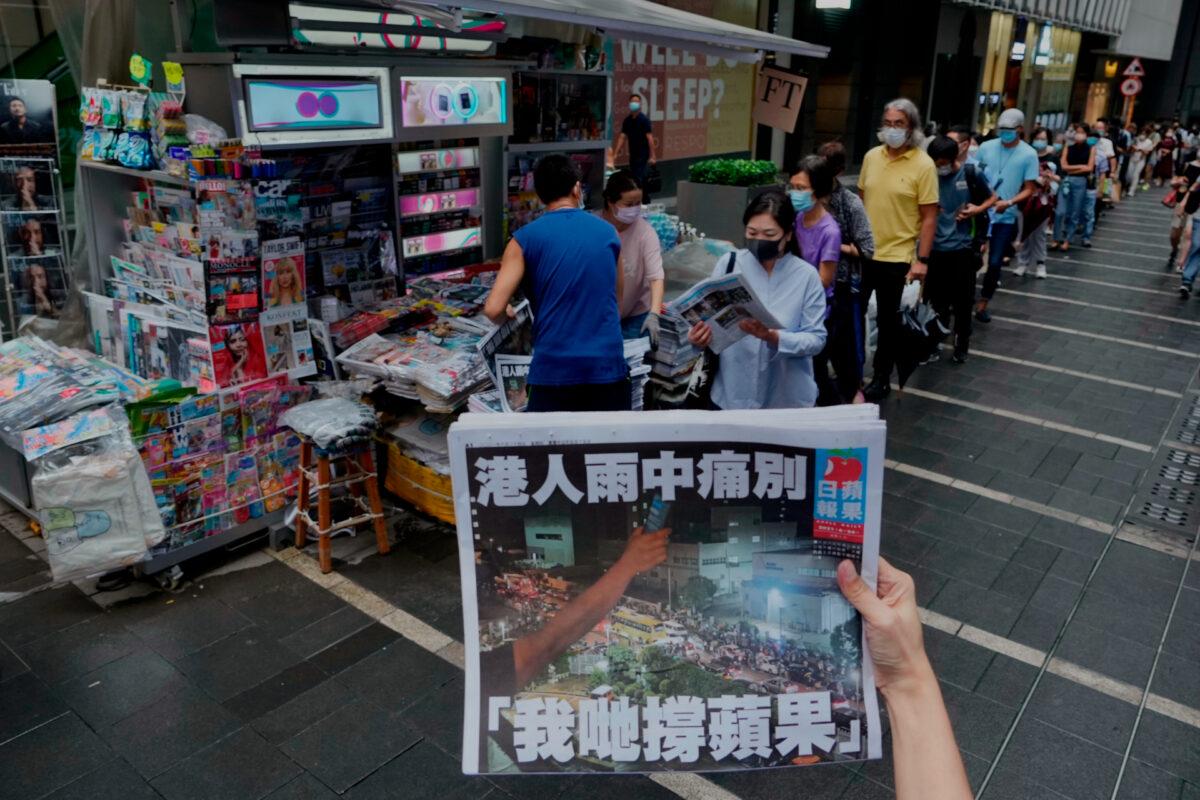 A woman takes a photo of the last issue of Apple Daily in front of a newspaper booth where people are queuing up to buy the newspaper, in downtown Hong Kong, on June 24, 2021. (AP Photo/Vincent Yu)