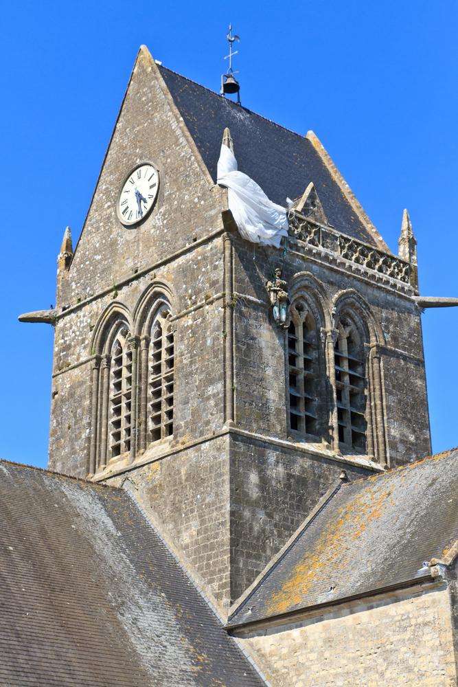 A mannequin of a paratrooper hanging from the church steeple in St. Mère-Eglise (Bertl123/Shutterstock)