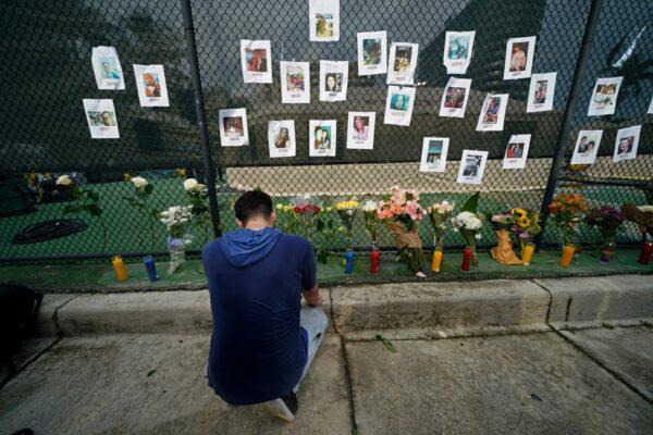 Leo Soto, who created this memorial with grocery stores donating flowers and candles, pauses in front of photos of some of the missing people that he put on a fence, near the site of an oceanfront condo building that partially collapsed in Surfside, Fla., on June 25, 2021. (Gerald Herbert/AP Photo)