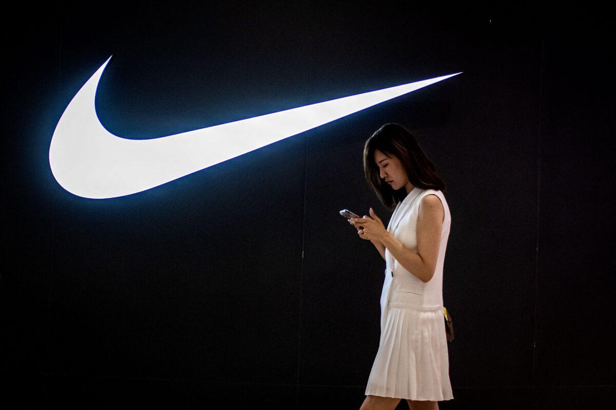A woman browses her phone while walking past a Nike logo inside a shopping mall in Beijing on June 2, 2021. (Nicolas Asfouri/AFP via Getty Images)