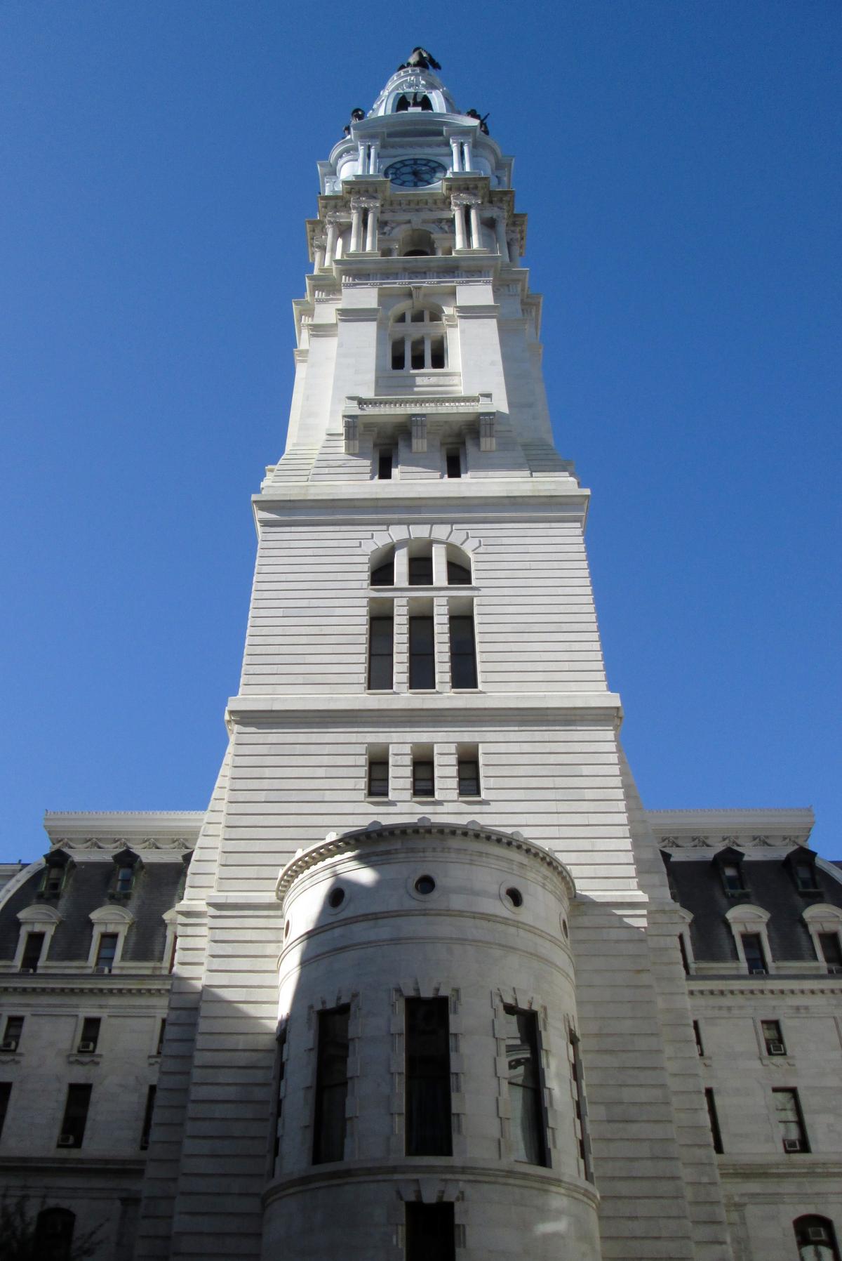 The most striking feature of the building is the large tower that rises high above the city floor. The body of the tower is restrained in comparison with the rest of the building. This leads the eye to the upper portions of the tower, where the columns, the large clocks, and an elongated dome form the pedestal for the statue of William Penn. (Beyond My Ken/CC BY-SA 4.0)