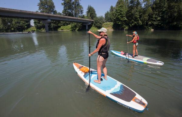 Susan Lange (L) and Debbie Thulen set off on inflatable paddle boards for a trip down the Stillaguamish River during record setting heat on in Arlington, Wash., on June 28, 2021. (Andy Bronson/The Herald via AP)