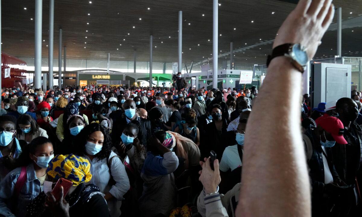 A protester raises his hand during a rally as passengers wait in front of the passport control of Terminal 2E of Charles de Gaulle Airport in Paris on July 2, 2021. (Thanassis Stavrakis/AP Photo)