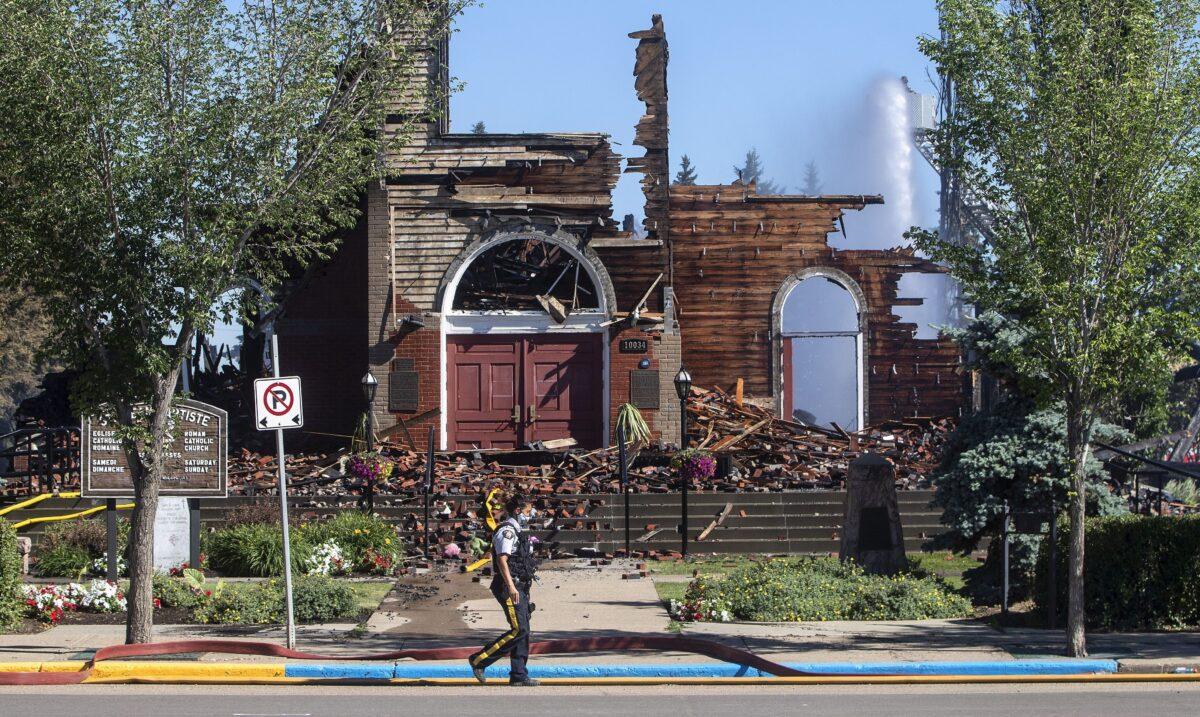 A police officer walks past what’s left of St. Jean Baptiste Parish Catholic church in Morinville, Alta., after it was burned down on June 30, 2021. (The Canadian Press/Jason Franso)
