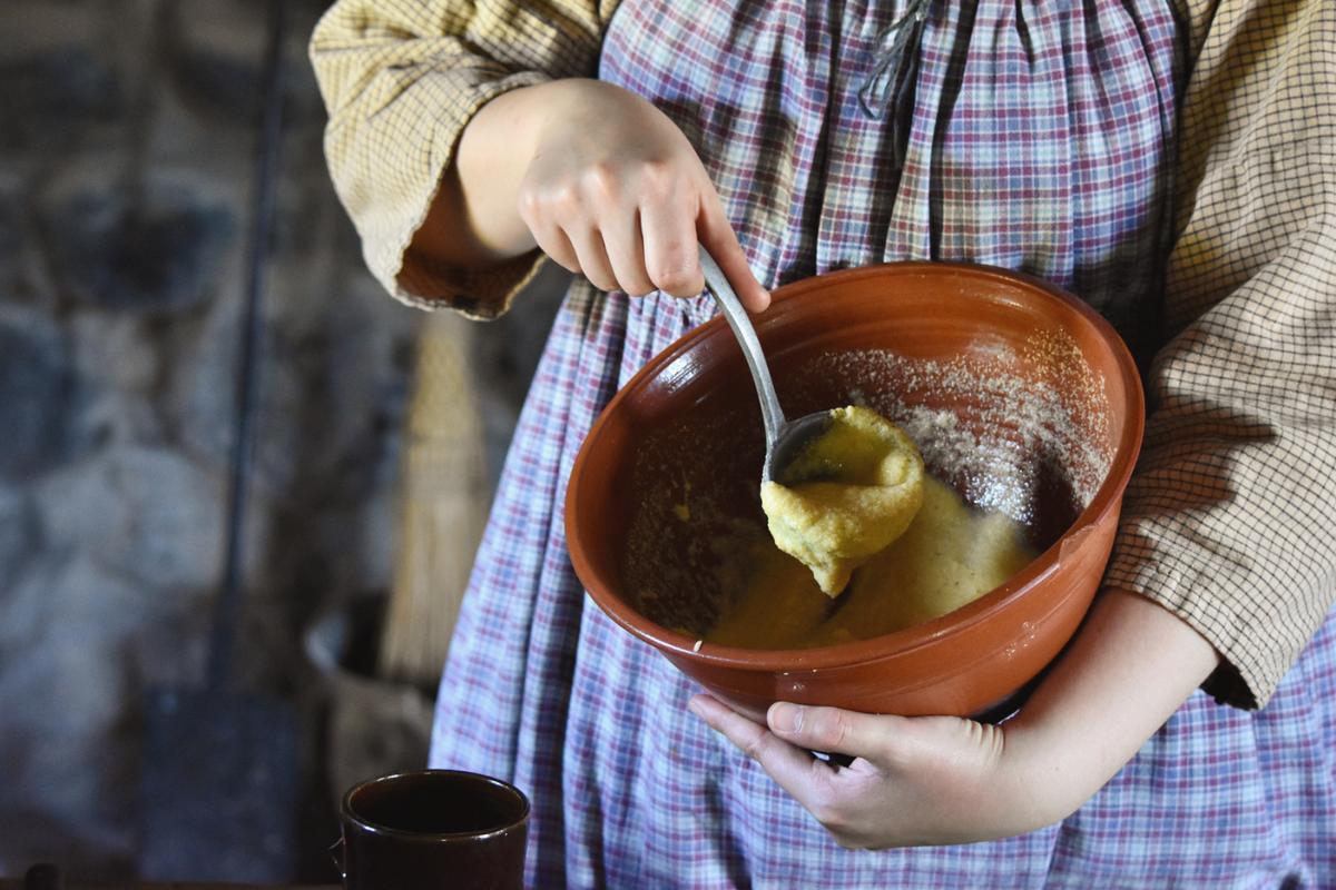A historic interpreter mixes up batter for johnny cakes to be cooked over a hearth in Hetchler House at Genesee Country Village & Museum. (Courtesy of Genesee Country Village & Museum)