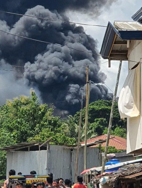 Residents gather as smoke rises from the wreckage, after a Philippine air force Lockheed C-130 transport plane, carrying troops, crashed on landing in Jolo, Sulu, Philippines, on July 4, 2021. (Bogs Muhajiran via Reuters)