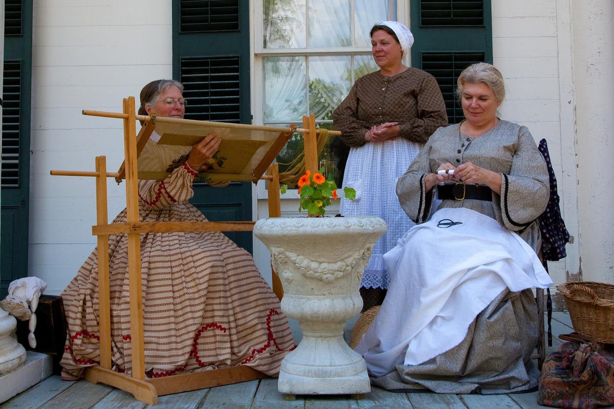 Interpreters on the porch of a historic home share traditional crafts with visitors at Genesee Country Village & Museum. (Courtesy of Genesee Country Village & Museum)
