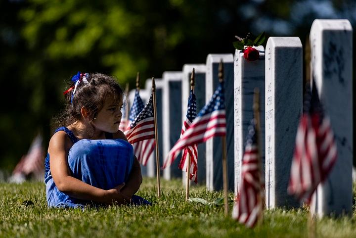 A girl sits in the grass amongst the headstones of those killed during the wars in Iraq and Afghanistan in Section 60 of Arlington National Cemetery in Arlington, Va., during Memorial Day on May 31, 2021. (Samuel Corum/Getty Images)