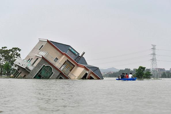 Residents ride a boat past a damaged and flood-affected house near the Poyang Lake due to torrential rains in Poyang county, Shangrao city in China's central Jiangxi Province, on July 15, 2020. (STR/AFP via Getty Images)