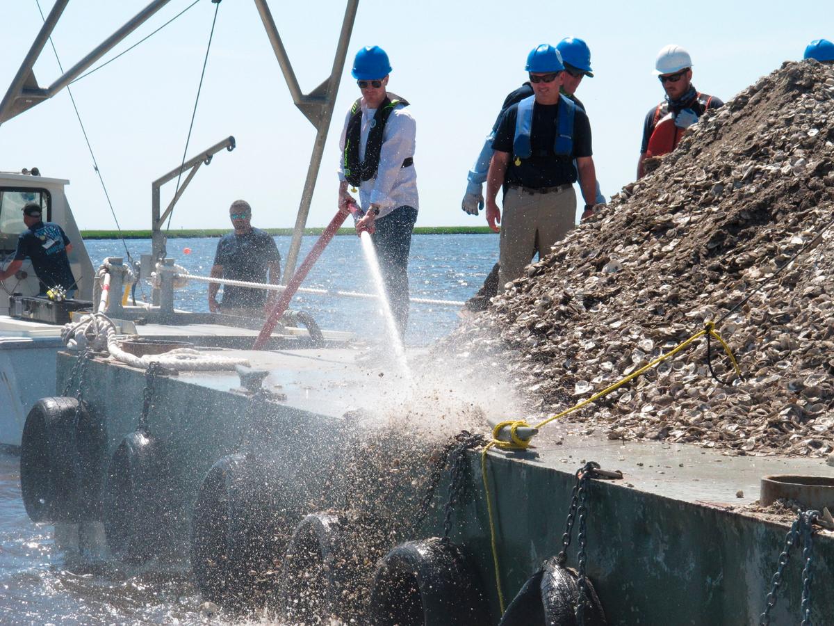 New Jersey Environmental Protection Commissioner Shawn LaTourette (L) uses a high-pressure hose to blast clam and oyster shells from the barge into the Mullica River. (AP Photo/Wayne Parry)