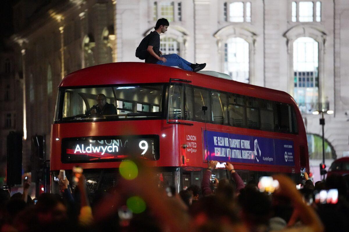 A man sits on top of a bus while England fans celebrate in Piccadilly Circus, central London, on July 7, 2021. (Kirsty O’Connor/PA)