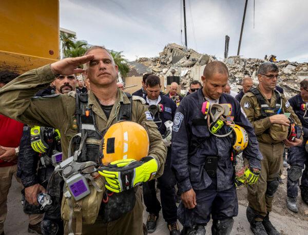 A member of the Israeli search and rescue team (L) salutes in front of the rubble that once was Champlain Towers South during a moment of prayer and silence in Surfside, Fla., on July 7, 2021. (JOSE A. IGLESIAS/POOL/AFP via Getty Images)